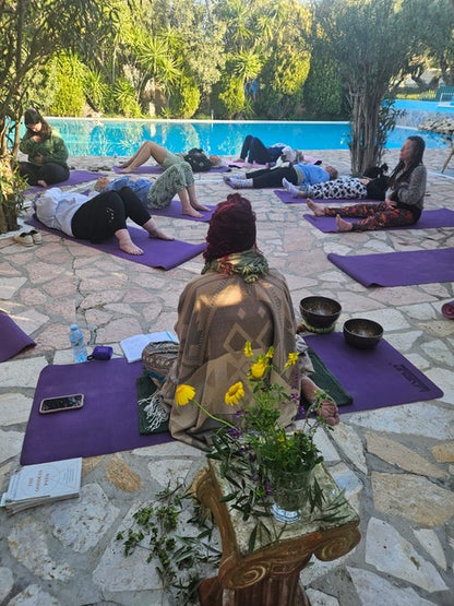 Group of people practicing yoga by a pool with a table holding flowers and books.