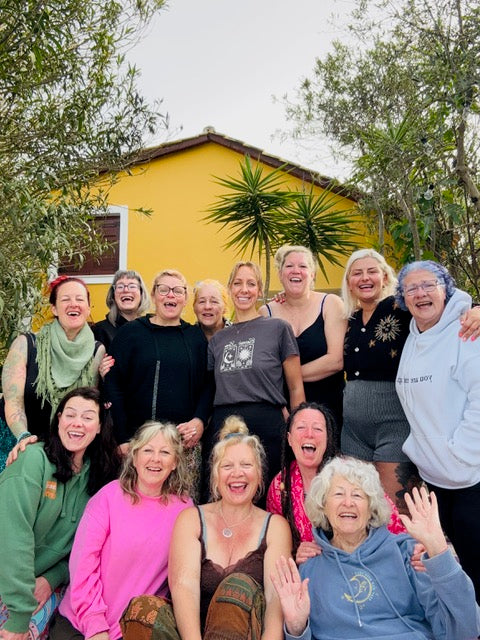 Group of women posing together outdoors with a yellow building and trees in the background