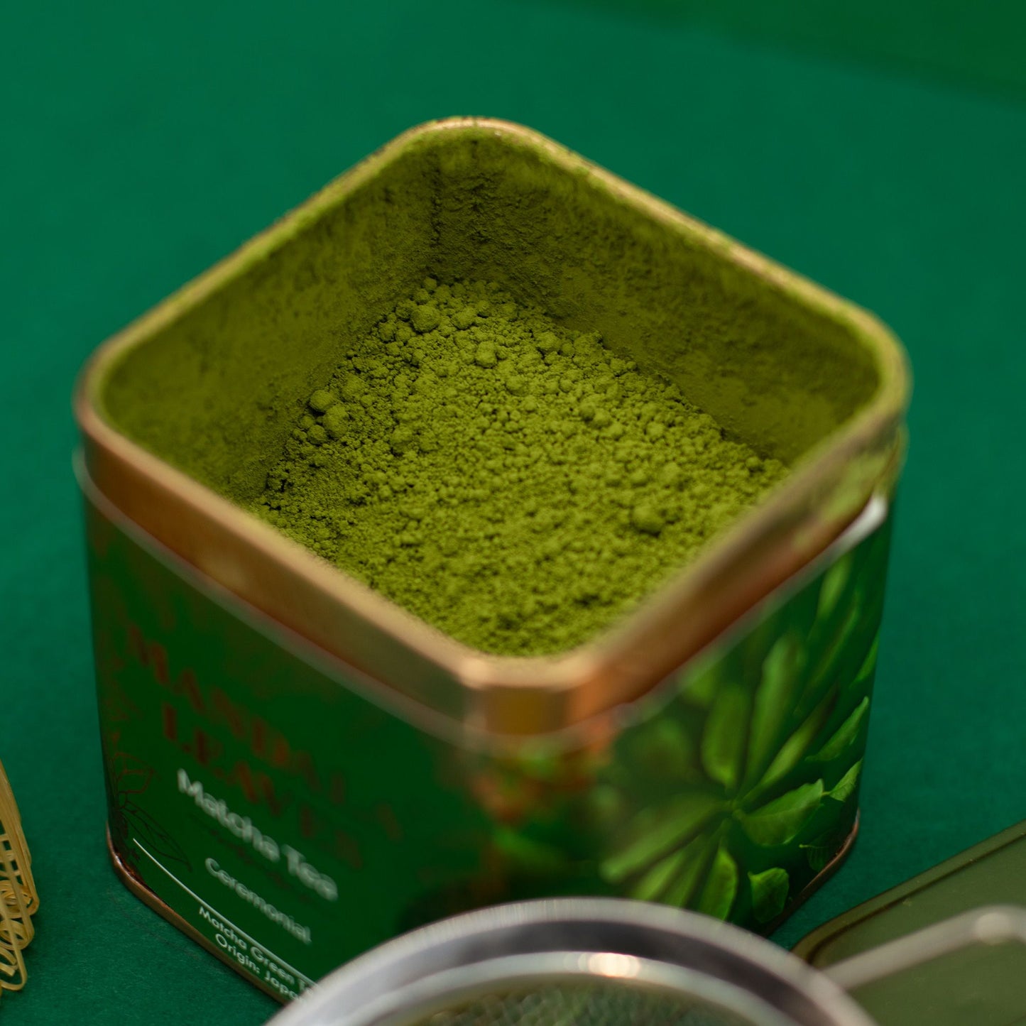 Open 50g ceremonial matcha tea tin, filled with vibrant green powder, on a green surface.