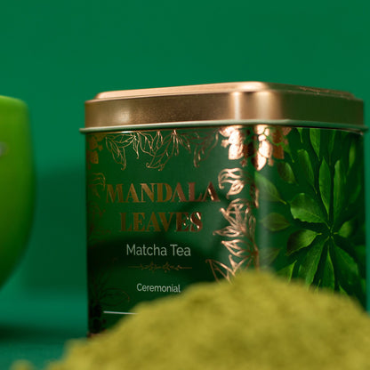 Green 50g Ceremonial Matcha Tea tin with gold lid and leaf design, next to a pile of matcha powder.